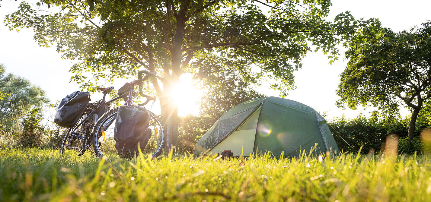 Urlaub mit Zelt und Rad geht auch spontan. Fahrrad mit Packtaschen und Zelt bei Sonnenuntergang.