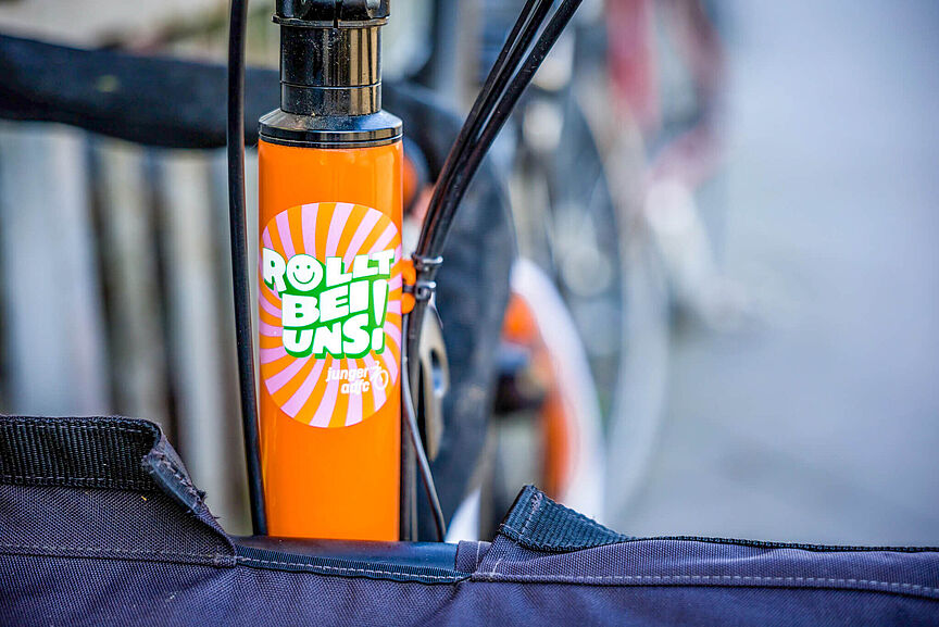 Junger ADFC Ein orangefarbener Fahrradrahmen mit einem bunten Aufkleber.