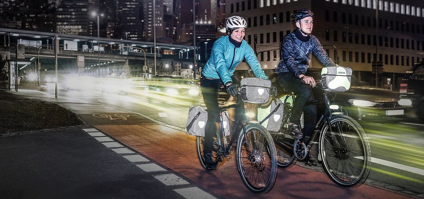 Eine Frau und ein Mann fahren bei Dunkelheit in der Stadt mit dem Rad. 